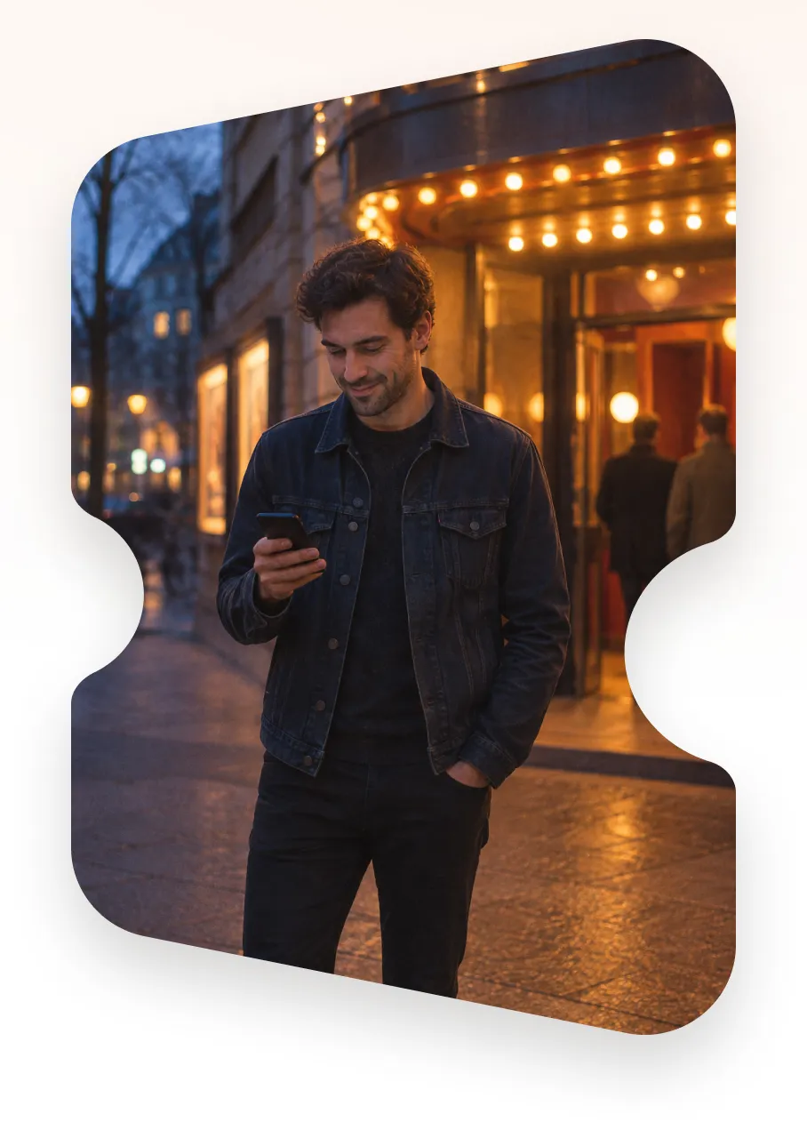 A visitor checking their phone outside a lit theatre entrance